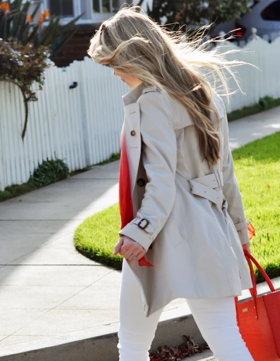 the blonde woman in a trench coat is walking down a street