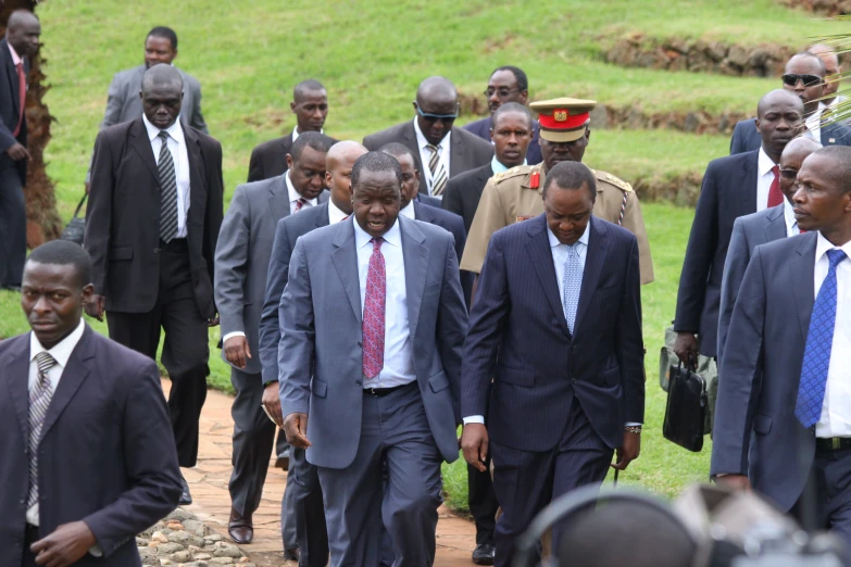 men walk together in suits with two red hats on