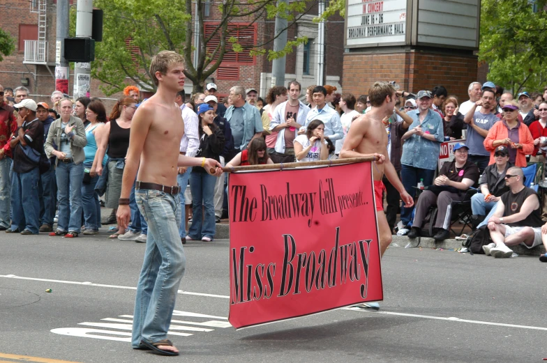 two shirtless guys carrying a large banner
