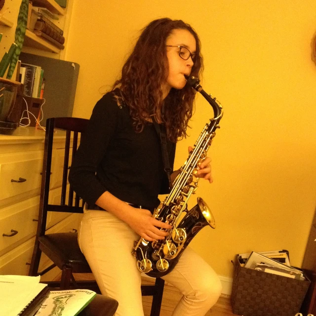 the woman is playing on the saxophone while sitting in a chair