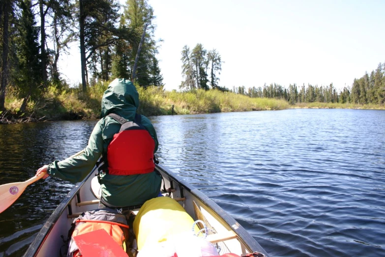 a man rows his canoe down a lake with trees in the background