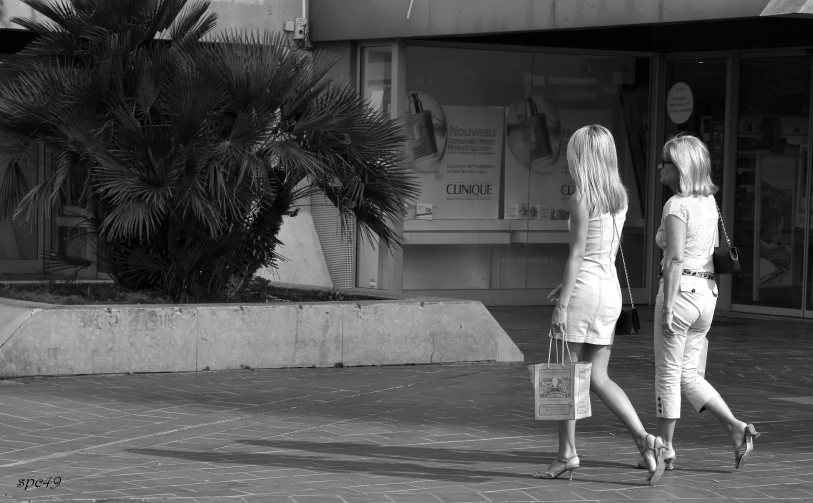 two young women walk down the sidewalk, in front of a building