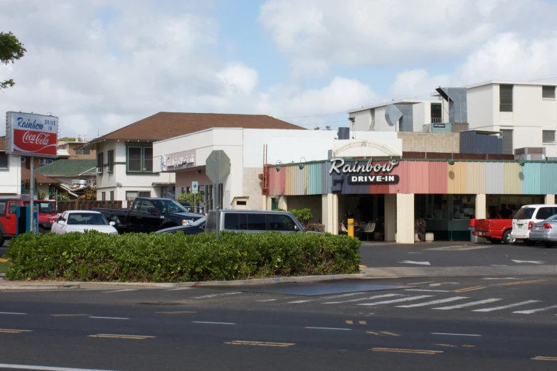 a street corner with parked cars on the side and many stores around it