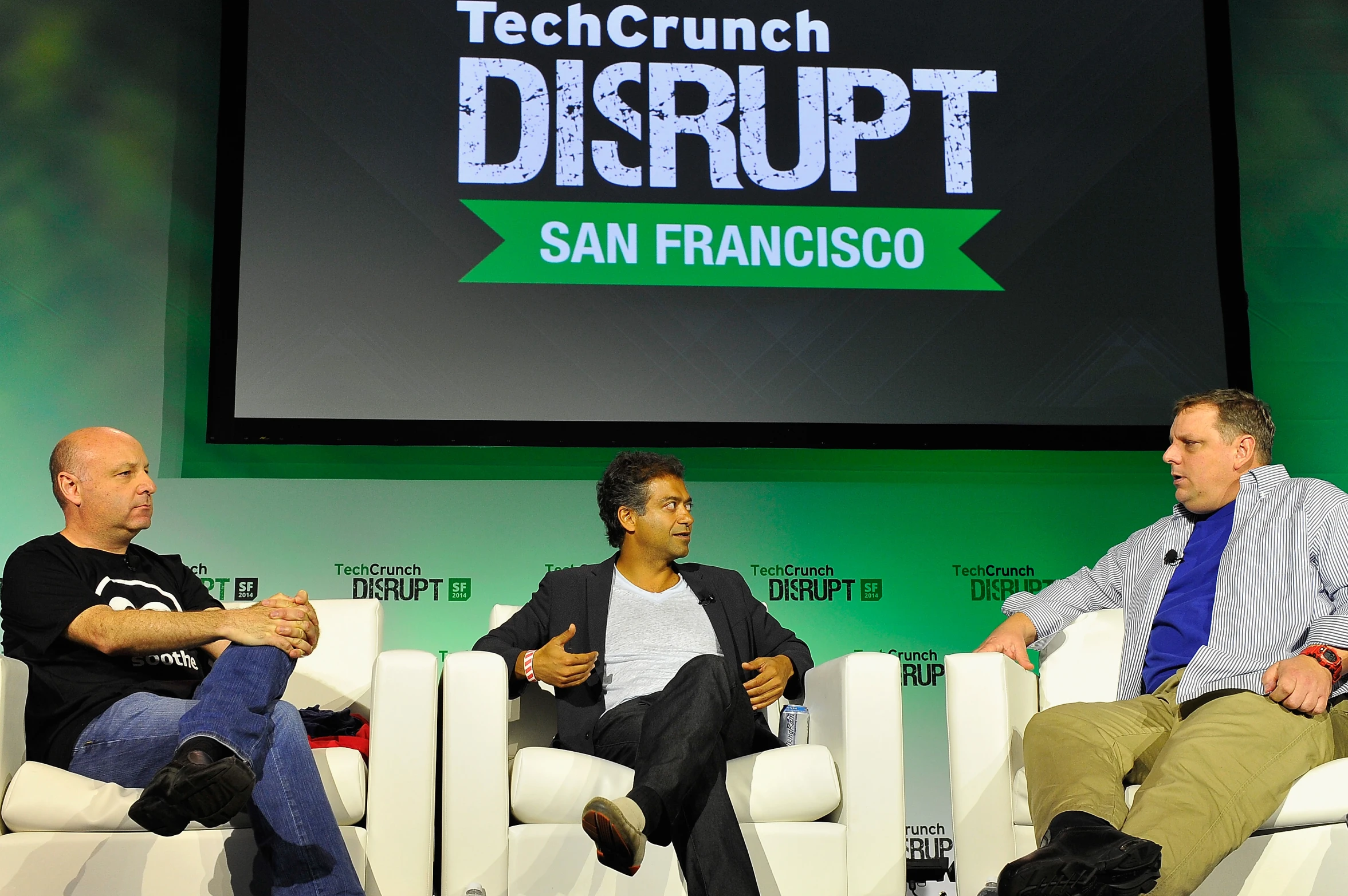 three people sit in chairs talking on stage at a techcrunch disrupt event