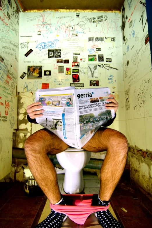 a man sitting on top of a toilet while reading the paper