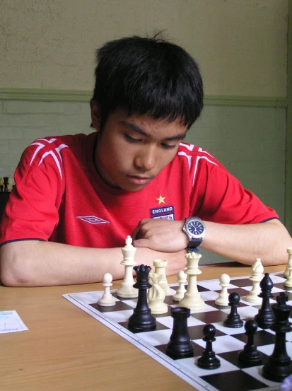 a boy looks down at the small black and white chess pieces