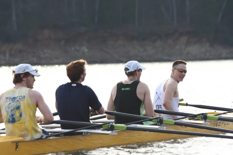 four men are standing on the edge of a yellow rowing boat