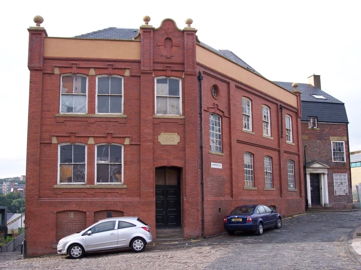 the two cars are parked in front of the large red brick building