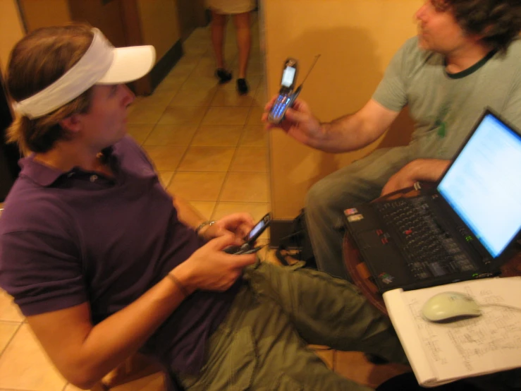 two people in a room sitting on the floor while one is holding a cell phone and the other has a laptop