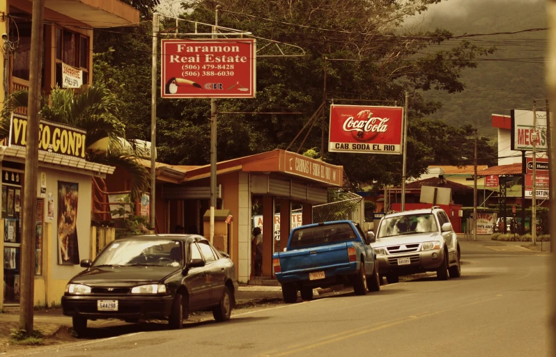 cars lined up along side a small street in front of businesses