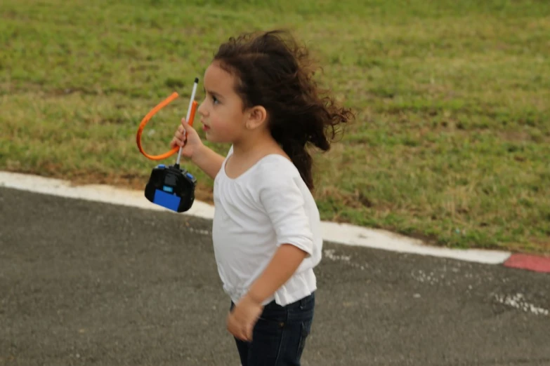 a small girl standing on top of a street holding an orange pair of scissors