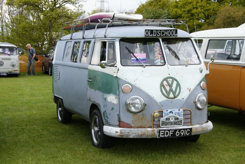 a volkswagen type bus sits parked on the grass with people around