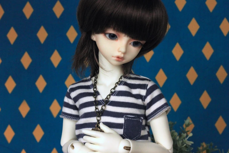 a doll wearing a dress and necklace next to a wall