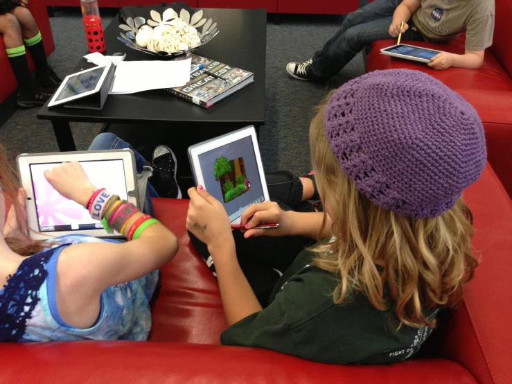 children using electronic devices on couches in a classroom