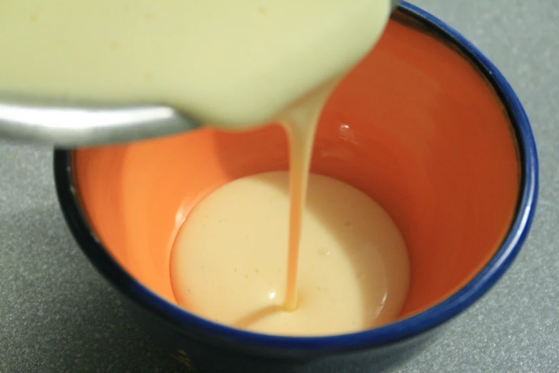 a spoon is pouring some orange juice in a bowl