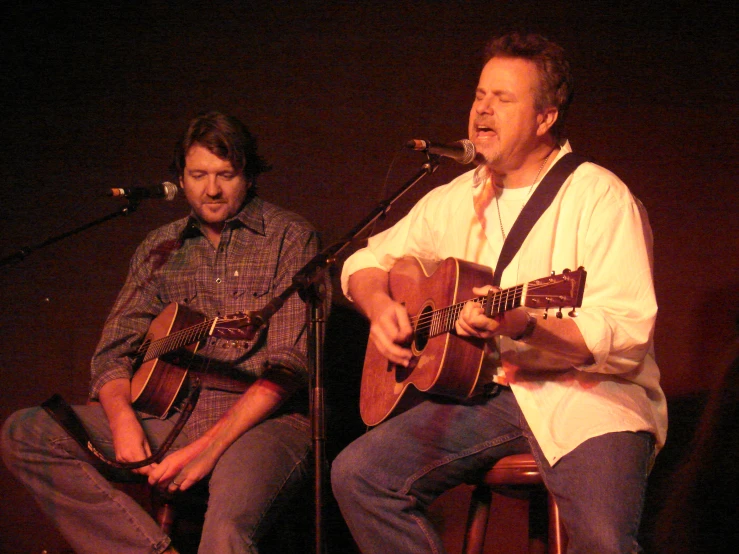 two men sitting on a chair while playing guitar