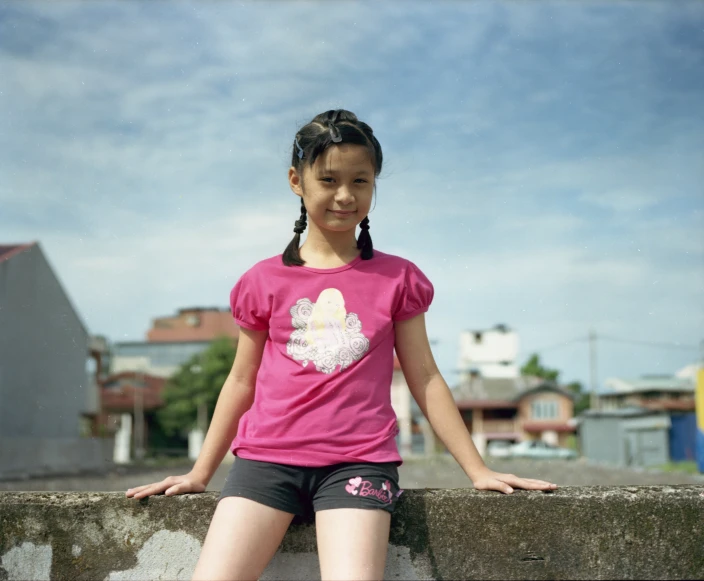 a little girl leaning against the fence in front of some buildings