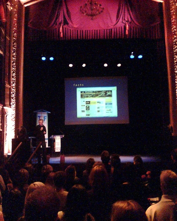 a man standing on stage giving a speech in front of a crowd