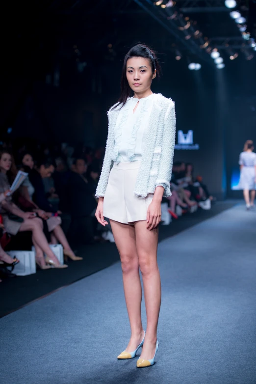 model standing on runway in white outfit with audience in the background