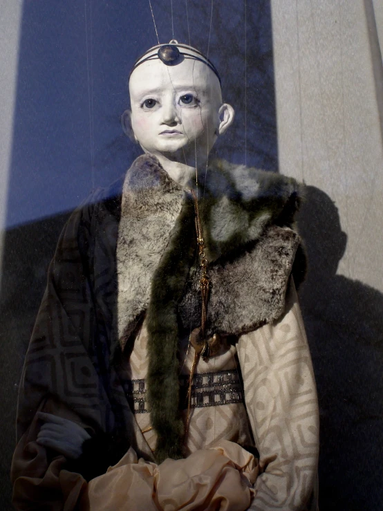 a white doll sitting under a window next to a curtain