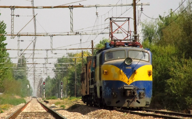 a blue train on railroad tracks with trees and people