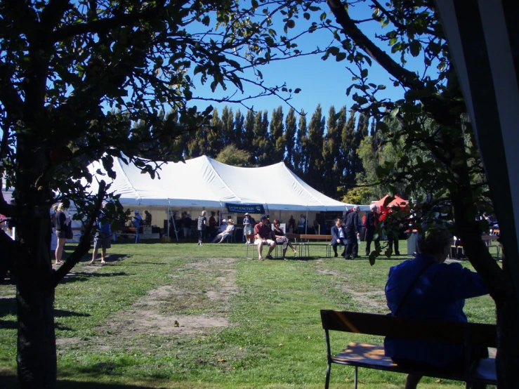 people are sitting on benches in a field under tents