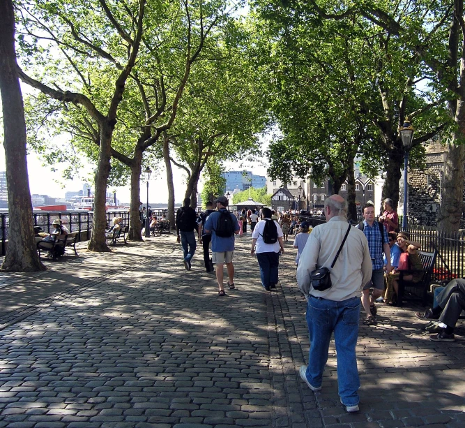 people walk down a brick walkway with benches along the path