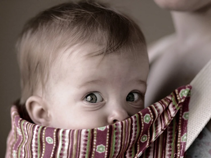 an adult holding a child with one eye showing and looking to the side