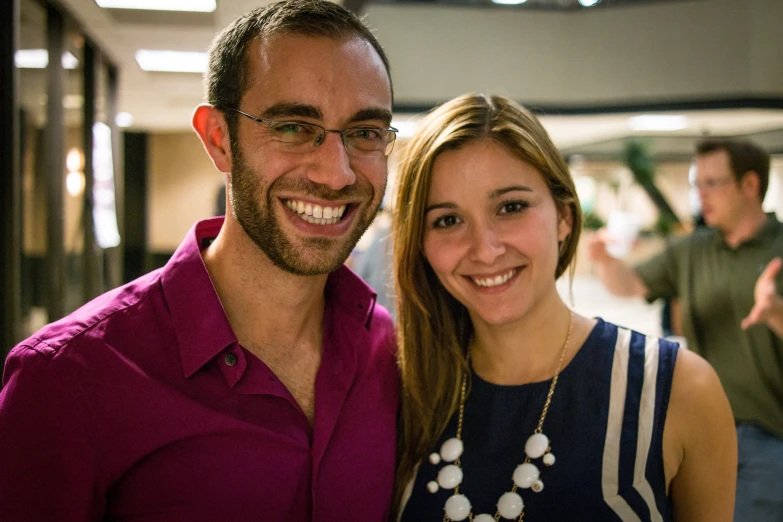 a man with long hair is standing next to a woman with glasses smiling at the camera