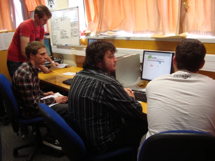 four young men sitting in front of computers in an office