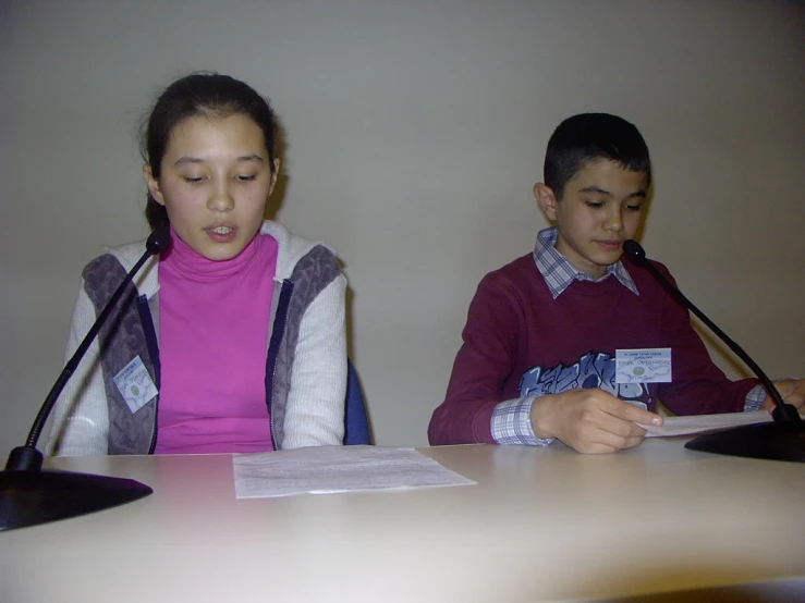 two s sit at a table while one of them looks on