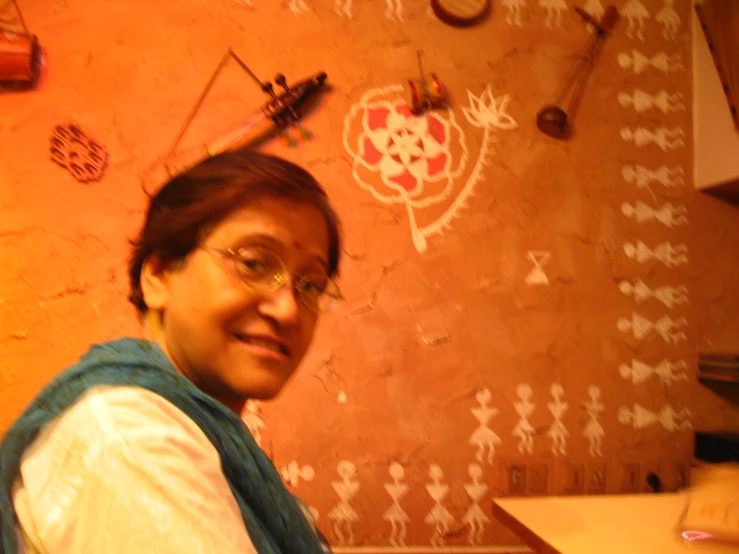 a lady wearing glasses and a vest in a room with wall decorations