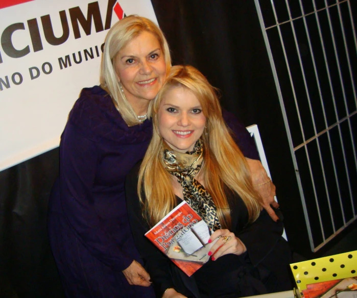 two women standing next to each other holding a book