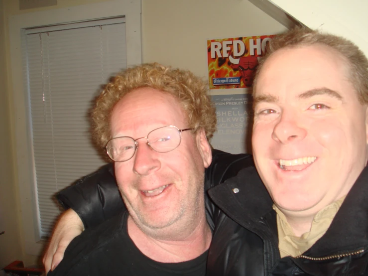 two men smiling while wearing glasses and jackets