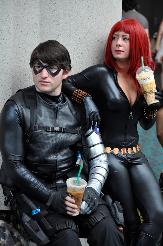 two people dressed in costumes holding beverages sit on a bench