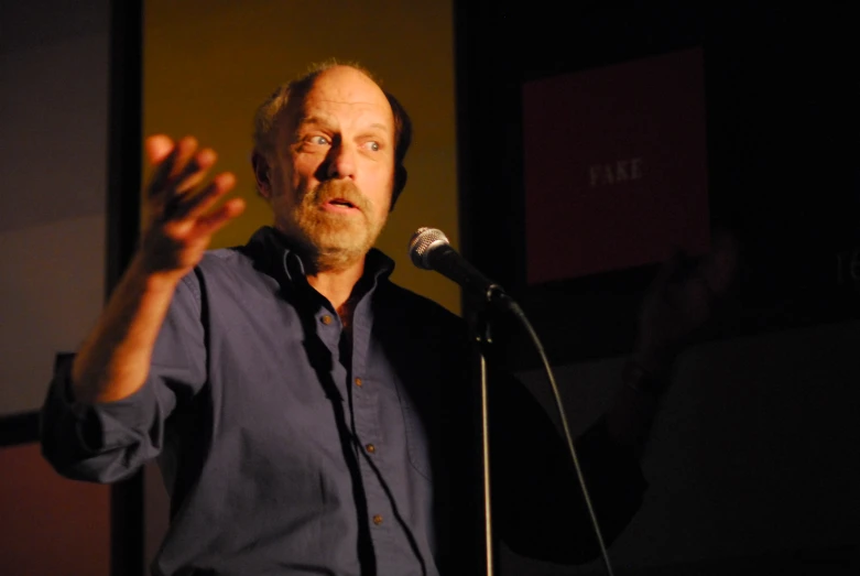 a man in a blue shirt with his hands up at a microphone