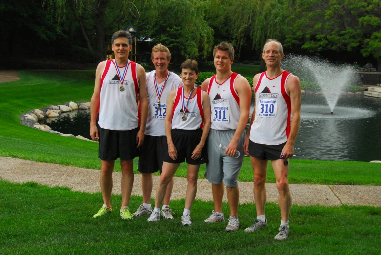 four people are wearing running bibs while standing in front of a fountain