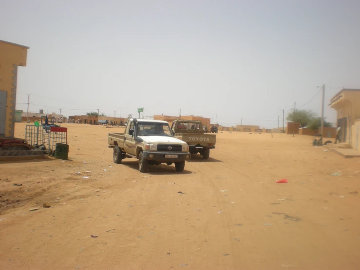 two trucks are parked in the dirt near some buildings