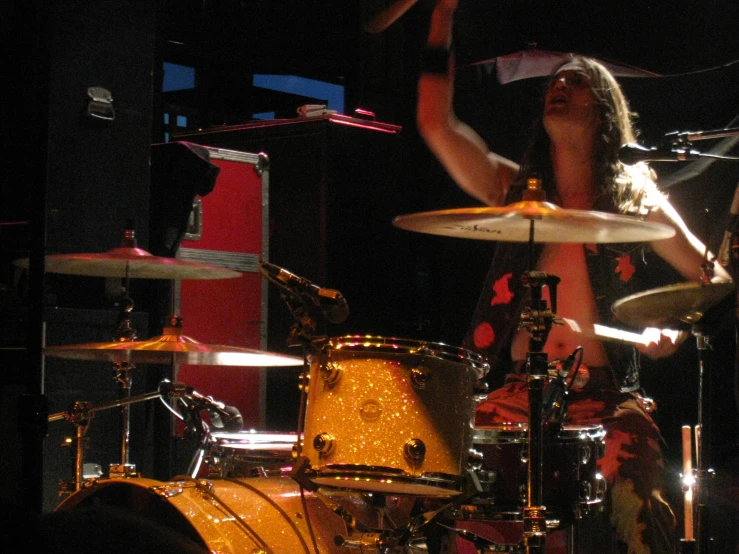 a woman sitting in front of drums holding her hands up