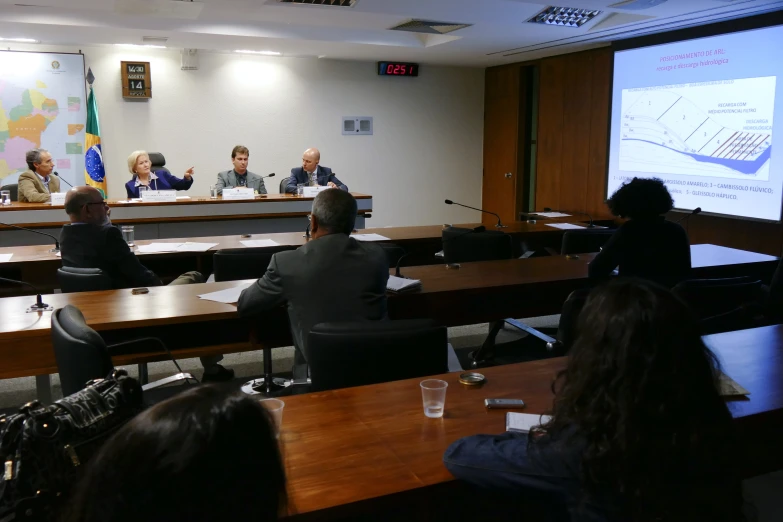 five people sitting in an empty meeting room as a woman speaks into a microphone