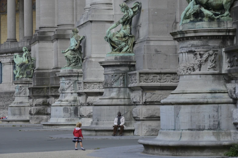 a woman stands in front of statues along side an old building