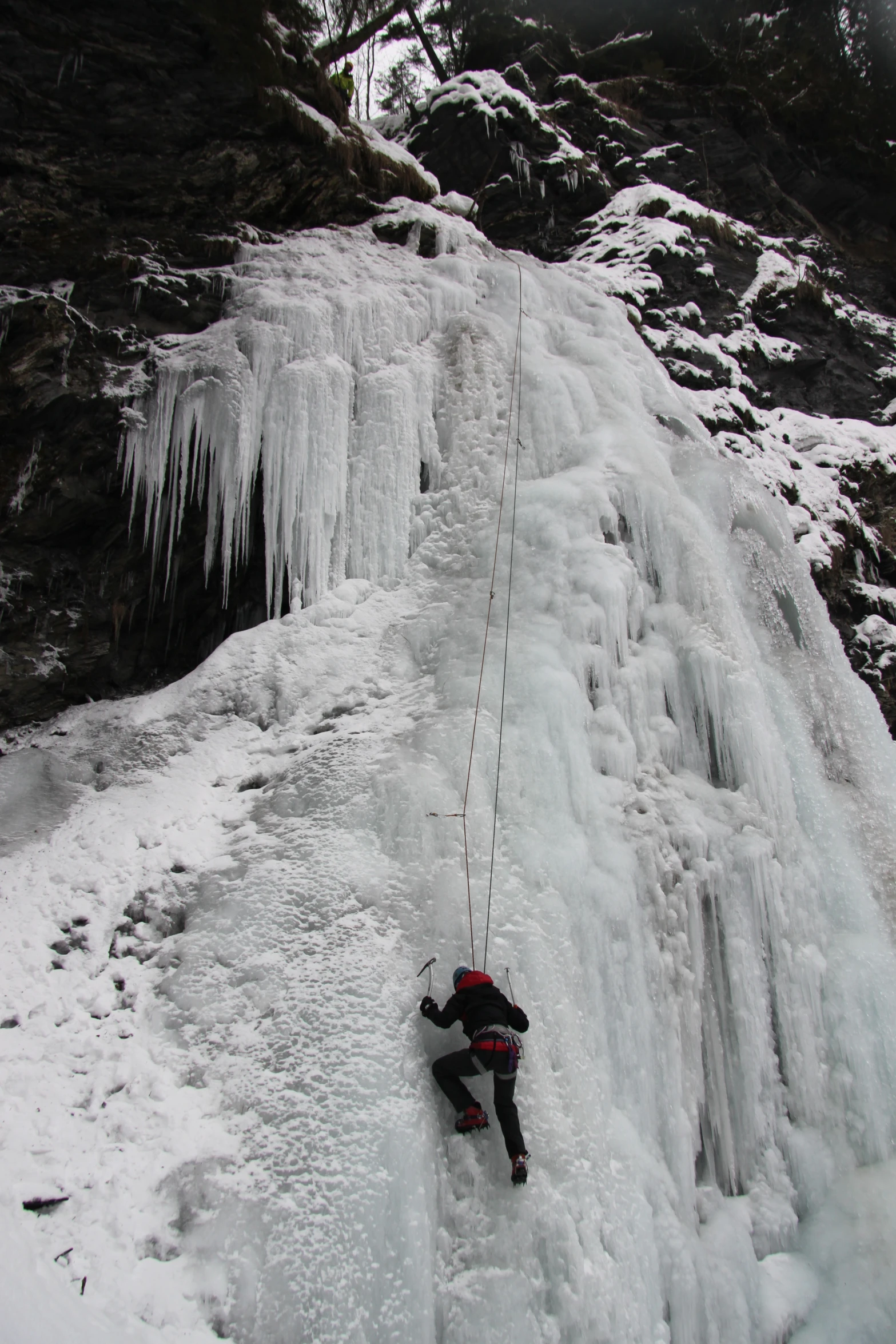 an ice climber climbs along a frozen waterfall