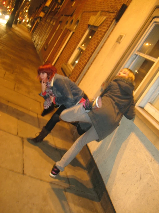 two young women, one holding onto the strap of a phone, are walking down a sidewalk