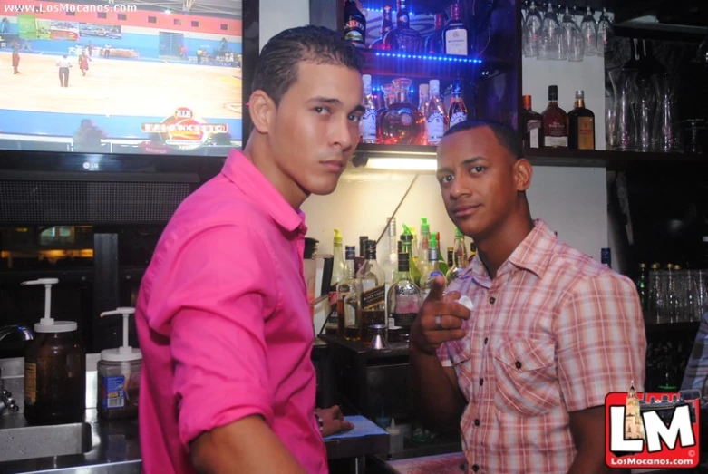 two men in shirts standing in front of the bar