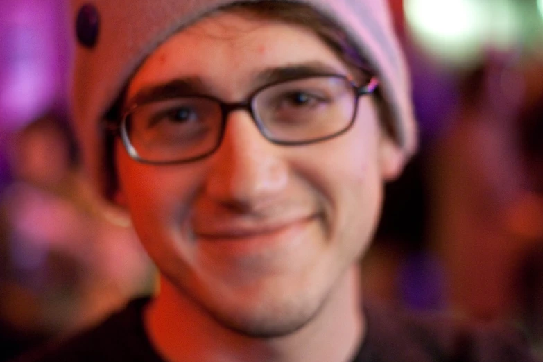 a man in a hat and glasses smiles at the camera