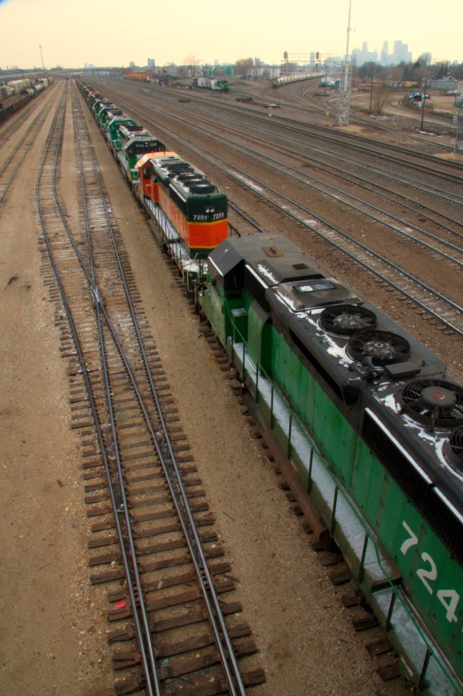 a green train pulling many other trains through a dry field