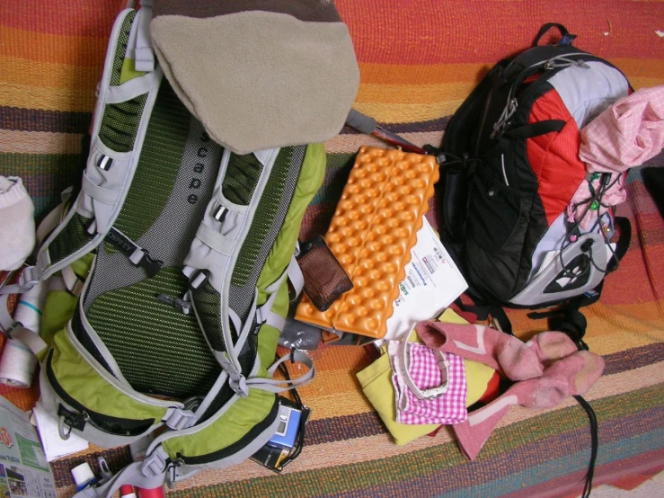a backpack with many items next to it on a blanket
