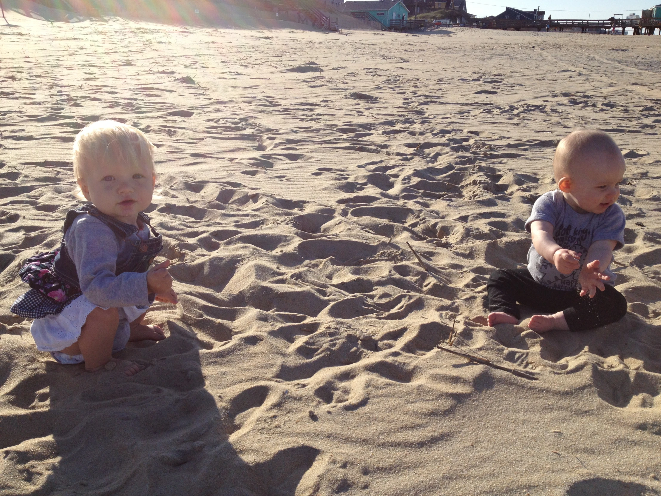 two babies sitting in the sand at a beach
