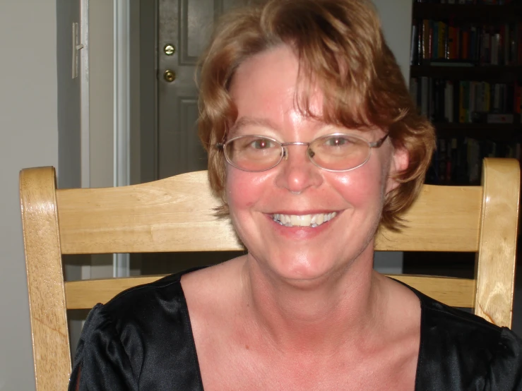 an older woman with glasses sitting in a chair smiling