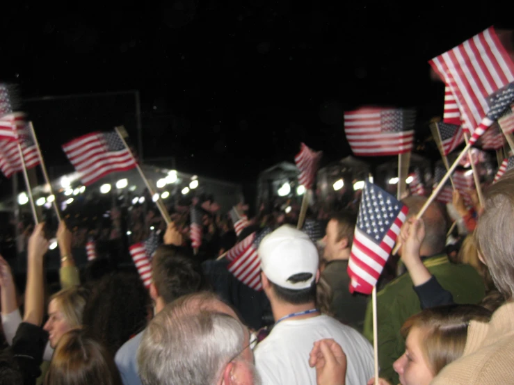 a large crowd holding american flags in the air